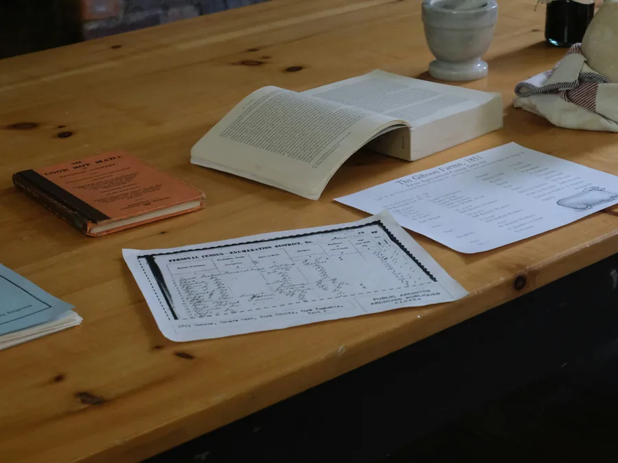 A researcher's desk with an open book, printed genealogical record forms, and reference materials on a wooden table.