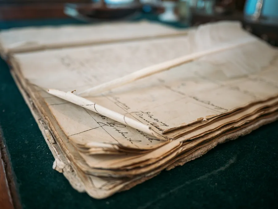 An aged bundle of handwritten documents tied with string, resting on a green baize desk surface with a quill stylus on top.